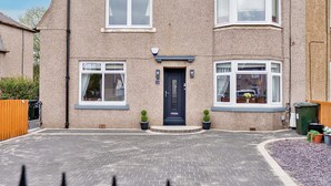 A two-story house with a dark front door, two windows on the ground floor, and a driveway leading to the entrance. - Bright and modern 2 bed flat with parking and a garden you can relax in (Edinburgh)