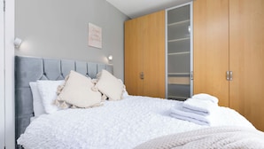 A neatly made bed with a grey headboard, white bedding, and a stack of white towels. - Bright and modern 2 bed flat with parking and a garden you can relax in (Edinburgh)