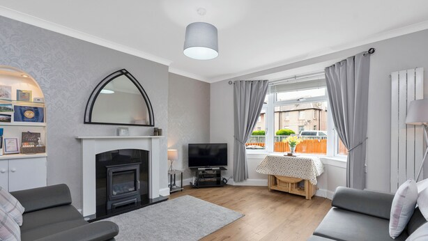 A modern living room with a fireplace, grey sofas, a flat-screen TV, and a view of the street. - Bright and modern 2 bed flat with parking and a garden you can relax in (Edinburgh)
