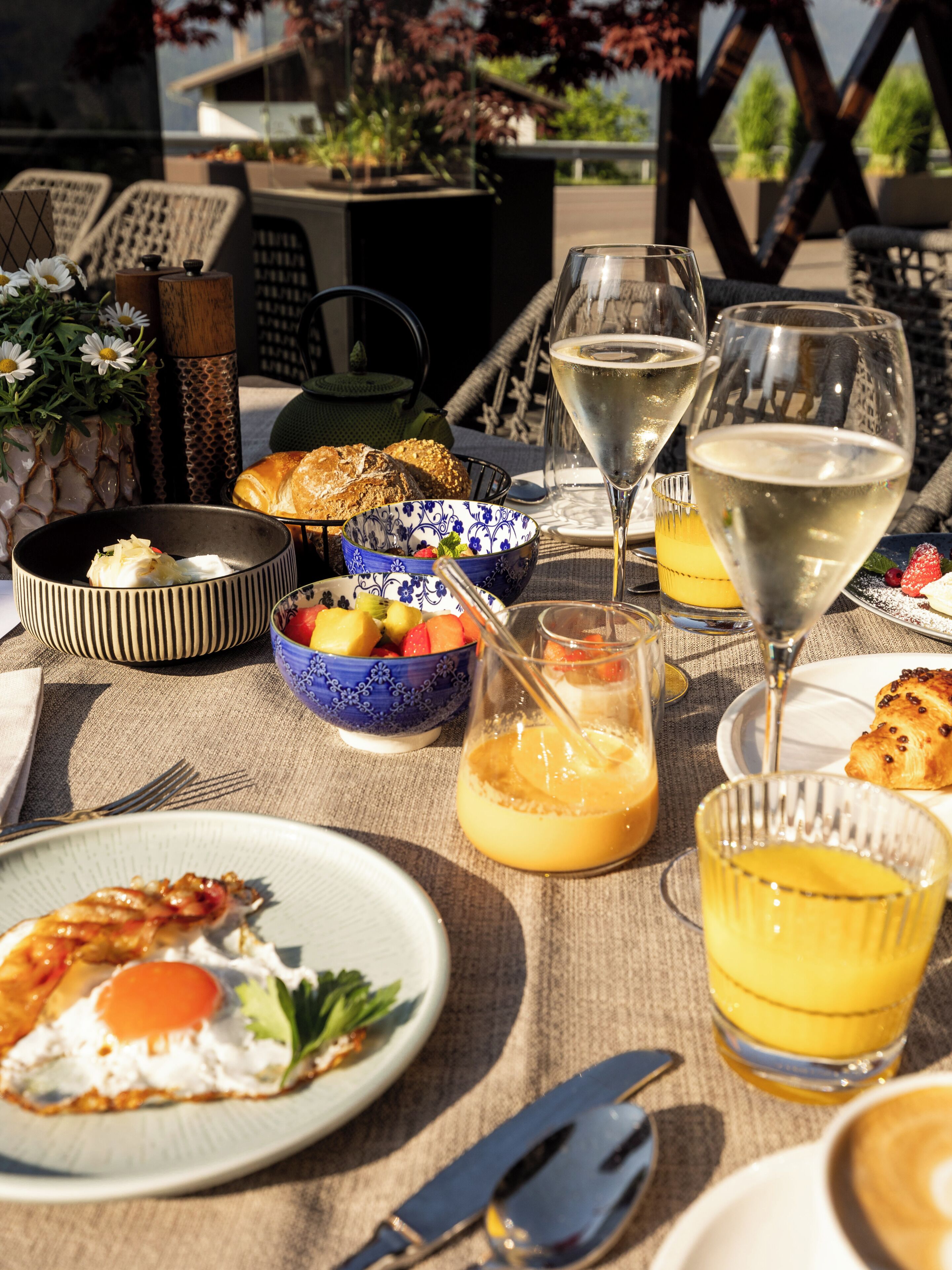 Ein Tisch ist reichhaltig mit Frühstücksleckereien gedeckt, darunter Eier, Toast und Obst, zusammen mit Gläsern Orangensaft und Weißwein.