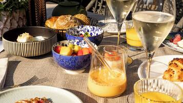 Ein Tisch ist reichhaltig mit Frühstücksleckereien gedeckt, darunter Eier, Toast und Obst, zusammen mit Gläsern Orangensaft und Weißwein.