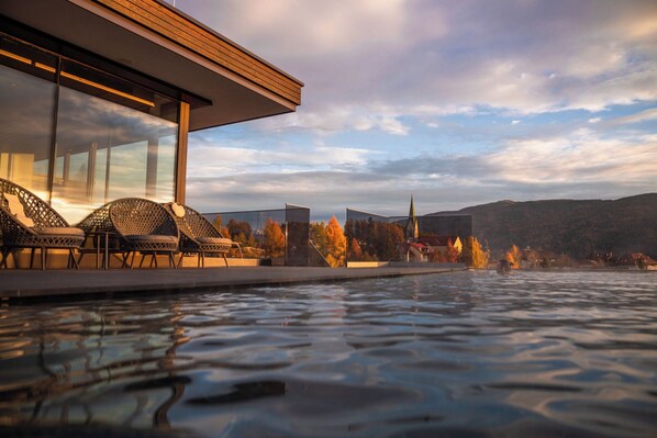A modern outdoor pool area with lounge chairs, a glass enclosure, and a view of a town and hills in the background.