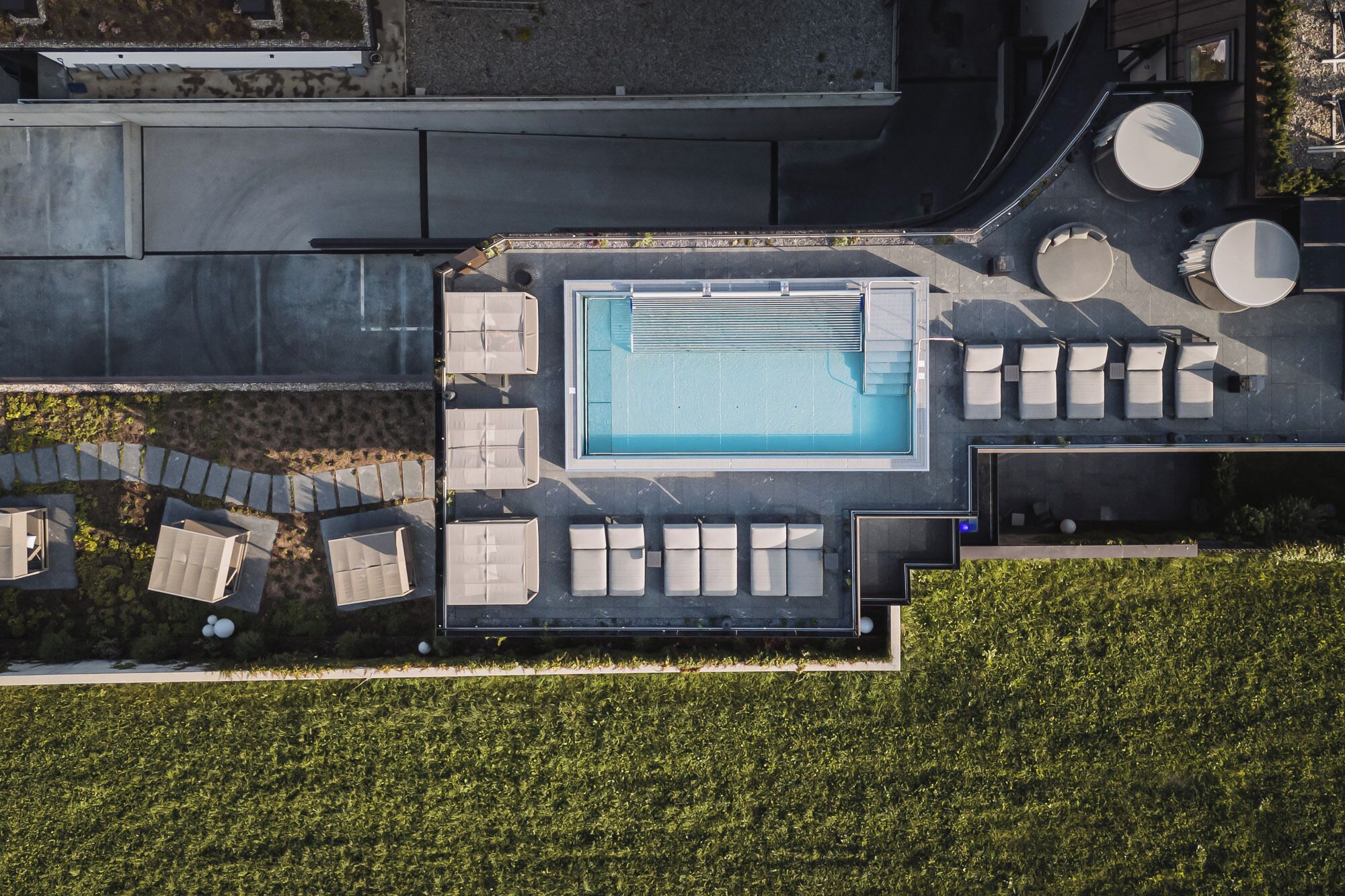 An aerial view of a modern pool area with a rectangular pool, multiple lounge chairs, and a small circular seating area.