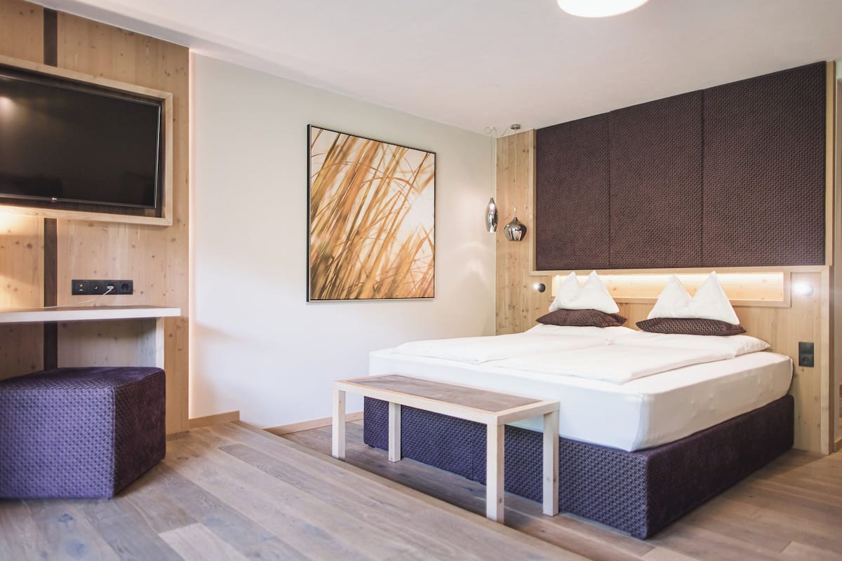 Een moderne slaapkamer met een bed, een bankje, een televisie en een aan de muur hangend kunstwerk.