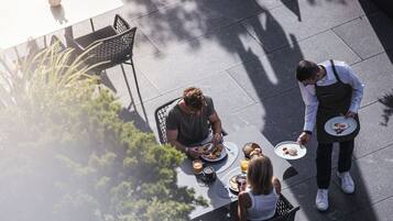 Un espacio al aire libre con zona de comedor, mesa, sillas y un camarero sirviendo comida.