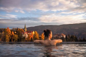 Une personne se détend dans une piscine, avec une vue sur la ville et les montagnes en arrière-plan.