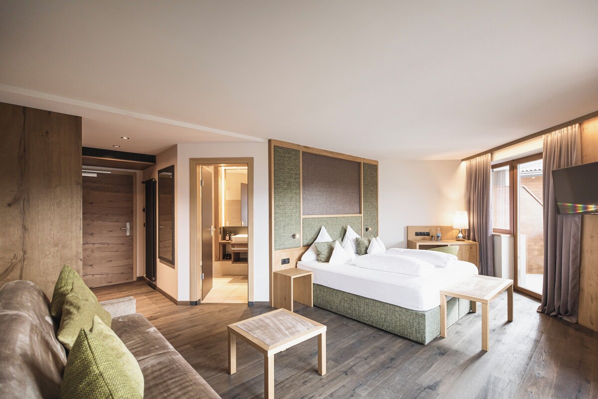 Ein modernes Hotelzimmer mit einem großen Bett, Holzboden, einer Couch, einem kleinen Tisch und einem Fernseher.