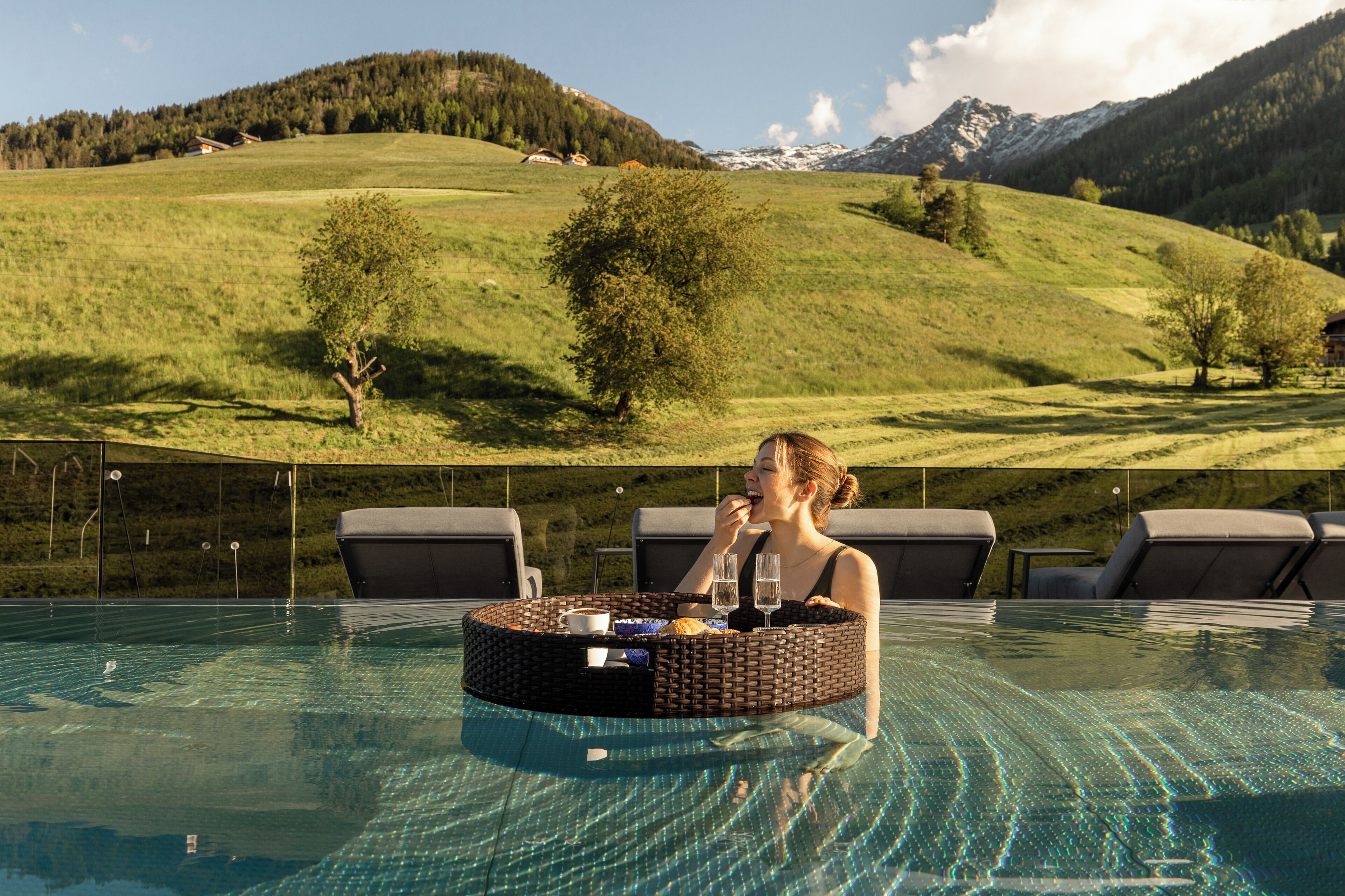 Zona de piscina con una silla de descanso, una mesa redonda con bandeja y vistas a un paisaje montañoso.