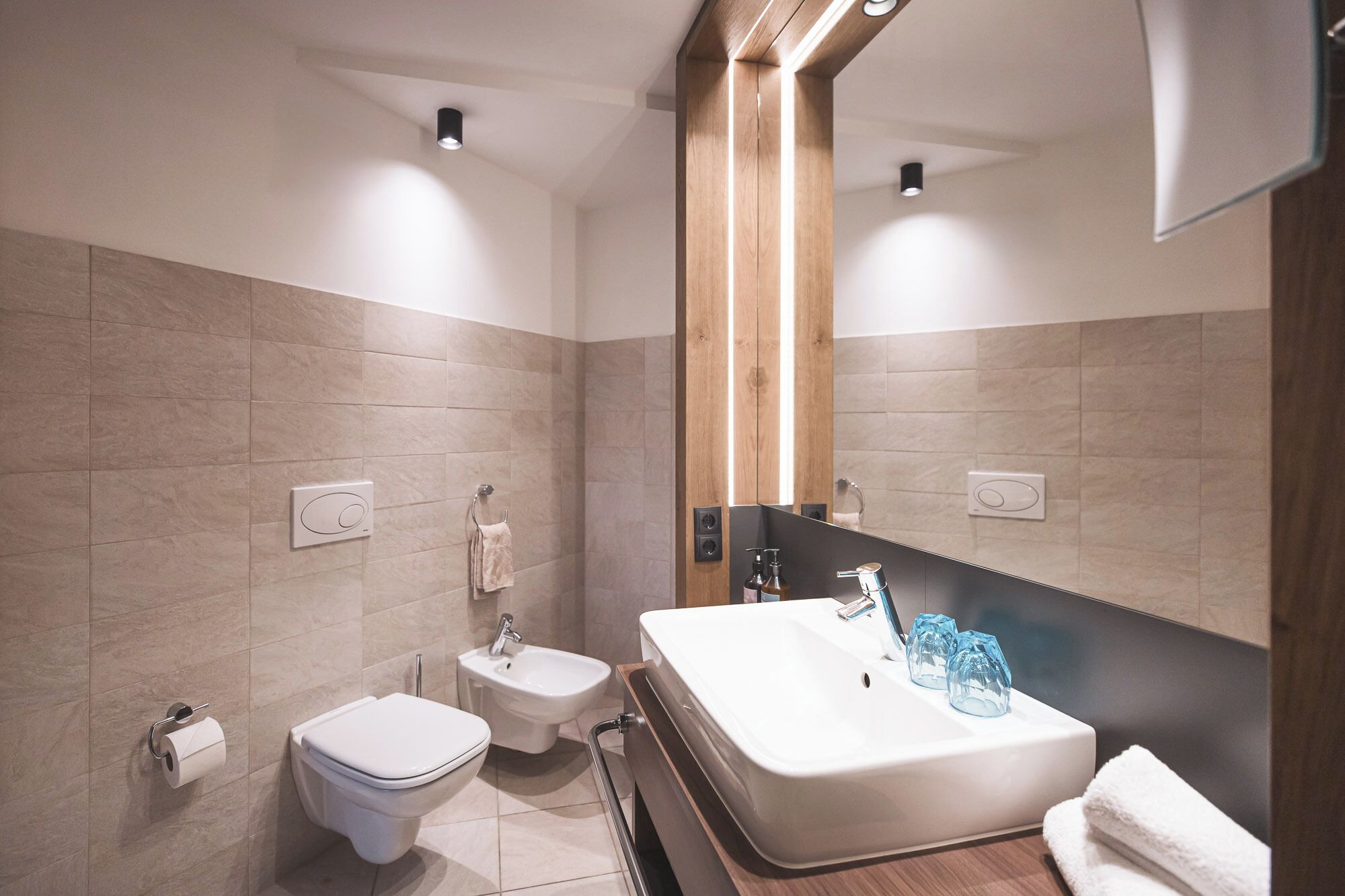 A modern bathroom with a toilet, bidet, and a large sink with a mirror.