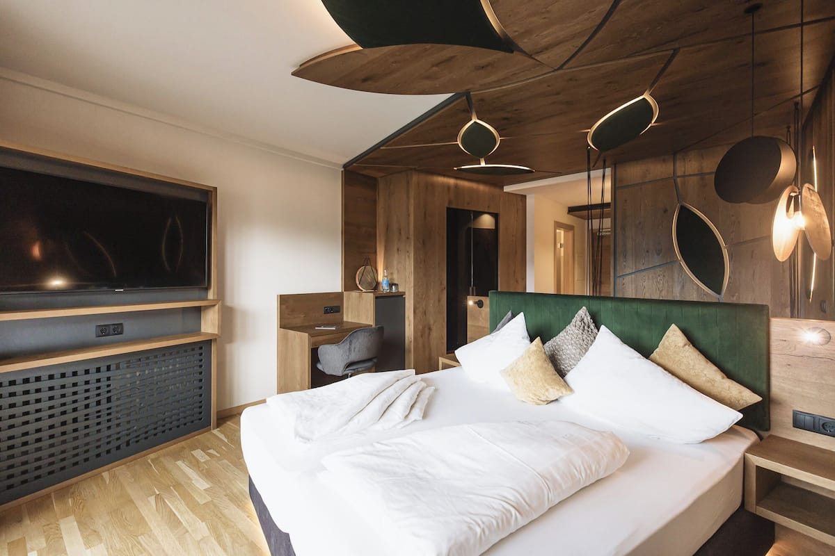 Een moderne slaapkamer met een groot bed, houten plafond en een televisie links.