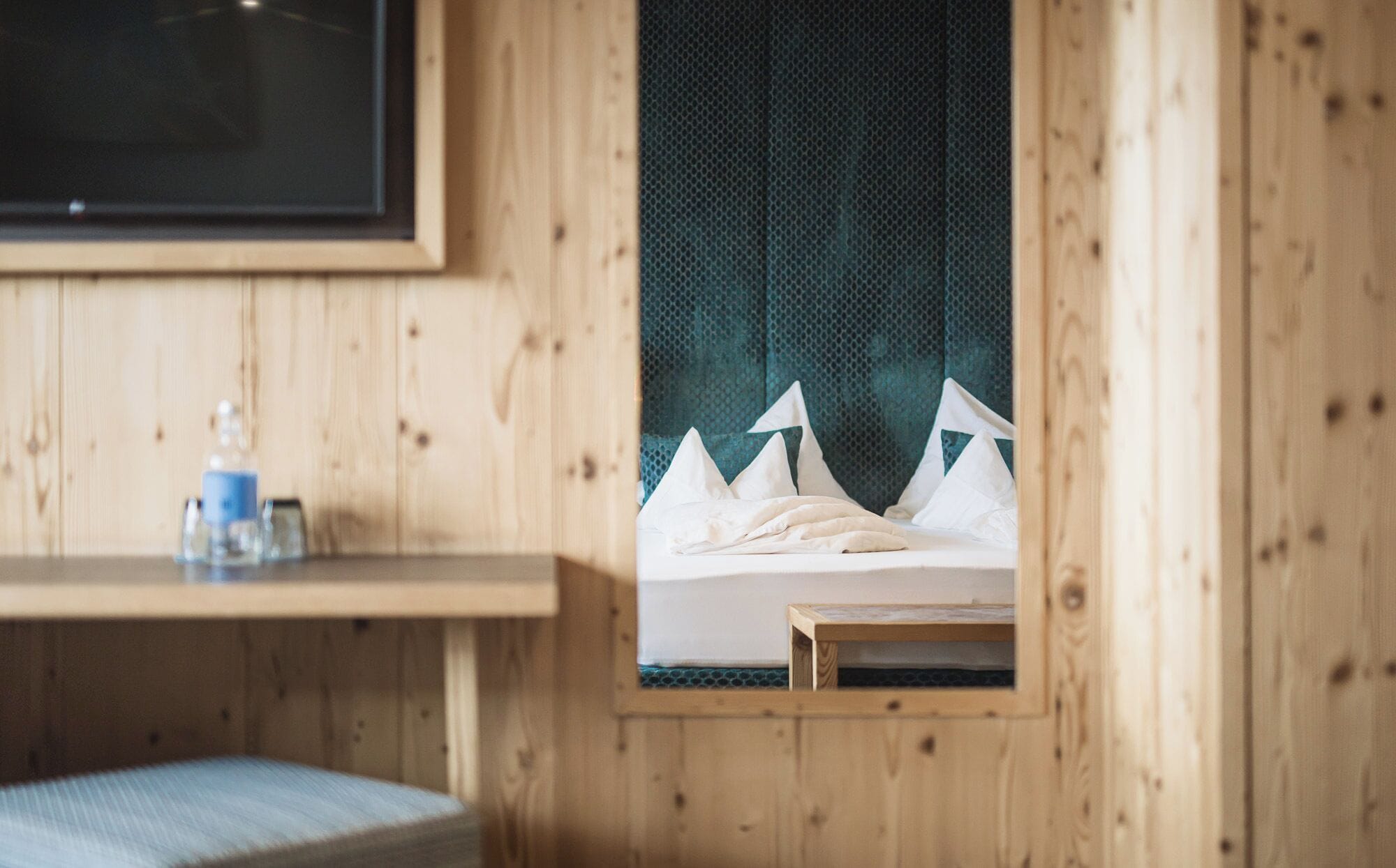 A wooden room with a bed, a small table, and a shelf with a bottle.