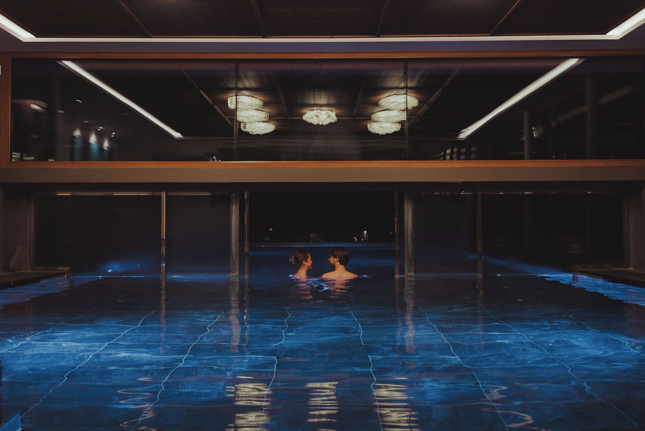 A large indoor swimming pool with a modern design, featuring a central area for socializing and a surrounding walkway.