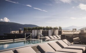 Ein Poolbereich auf dem Dach mit Liegestühlen und Blick auf Berge.