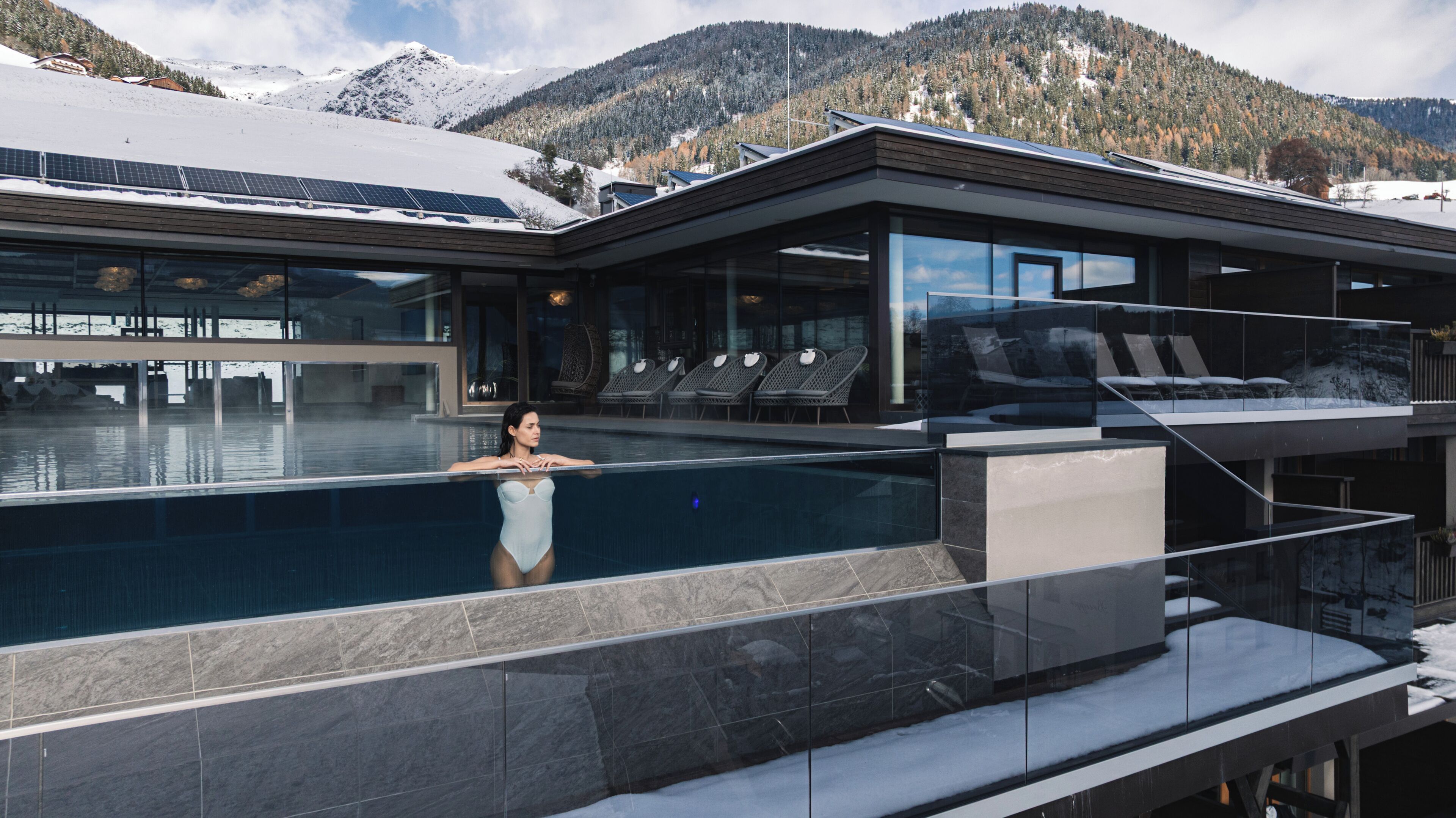 Un bâtiment moderne doté d’une piscine, de chaises longues et offrant une vue sur des montagnes enneigées.