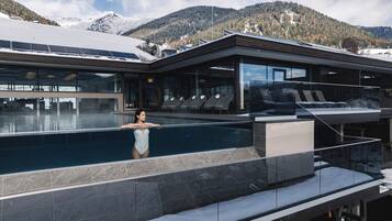 Un bâtiment moderne doté d’une piscine, de chaises longues et offrant une vue sur des montagnes enneigées.