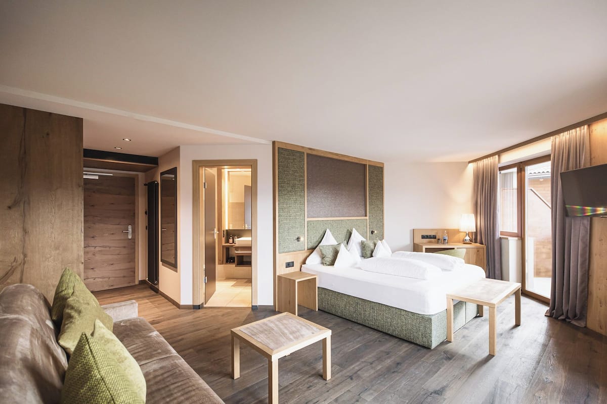 Een moderne hotelkamer met een groot bed, een houten hoofdbord, een klein tafeltje, een bank en een televisie.