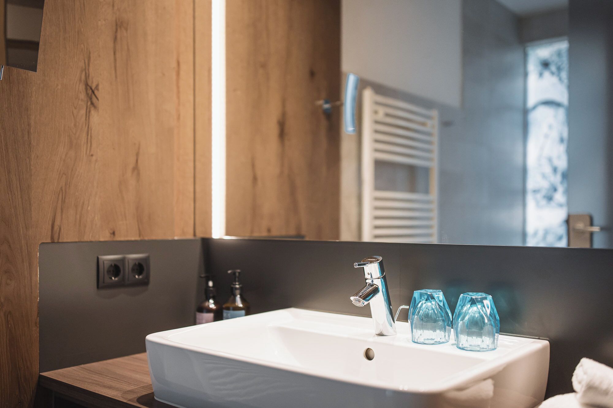 Ein modernes Badezimmer mit einem weißen Waschbecken, einem chromfarbenen Wasserhahn und zwei klaren Gläsern.