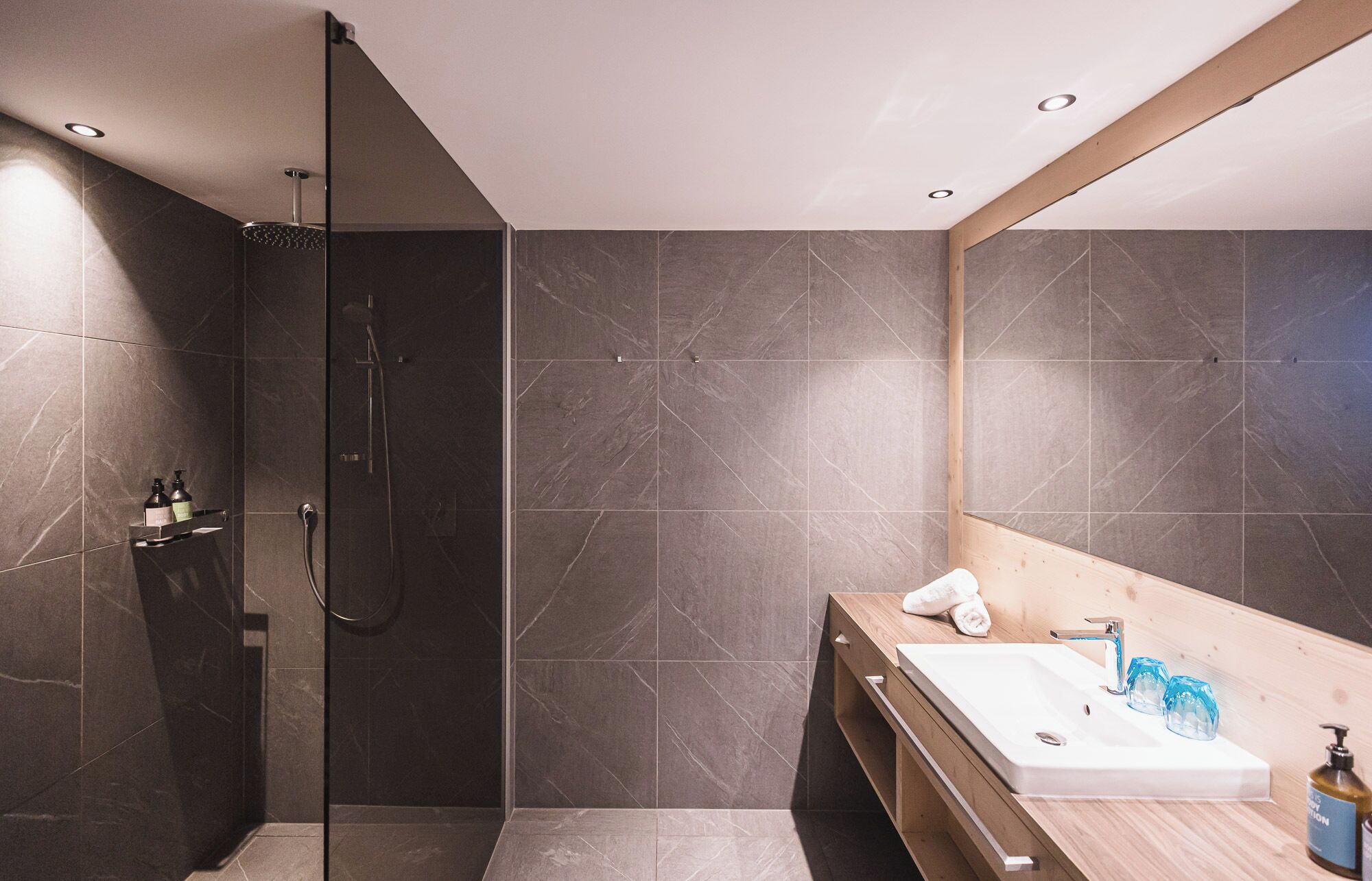 A modern bathroom with a glass-enclosed shower, a wooden vanity with a sink, and a large mirror.