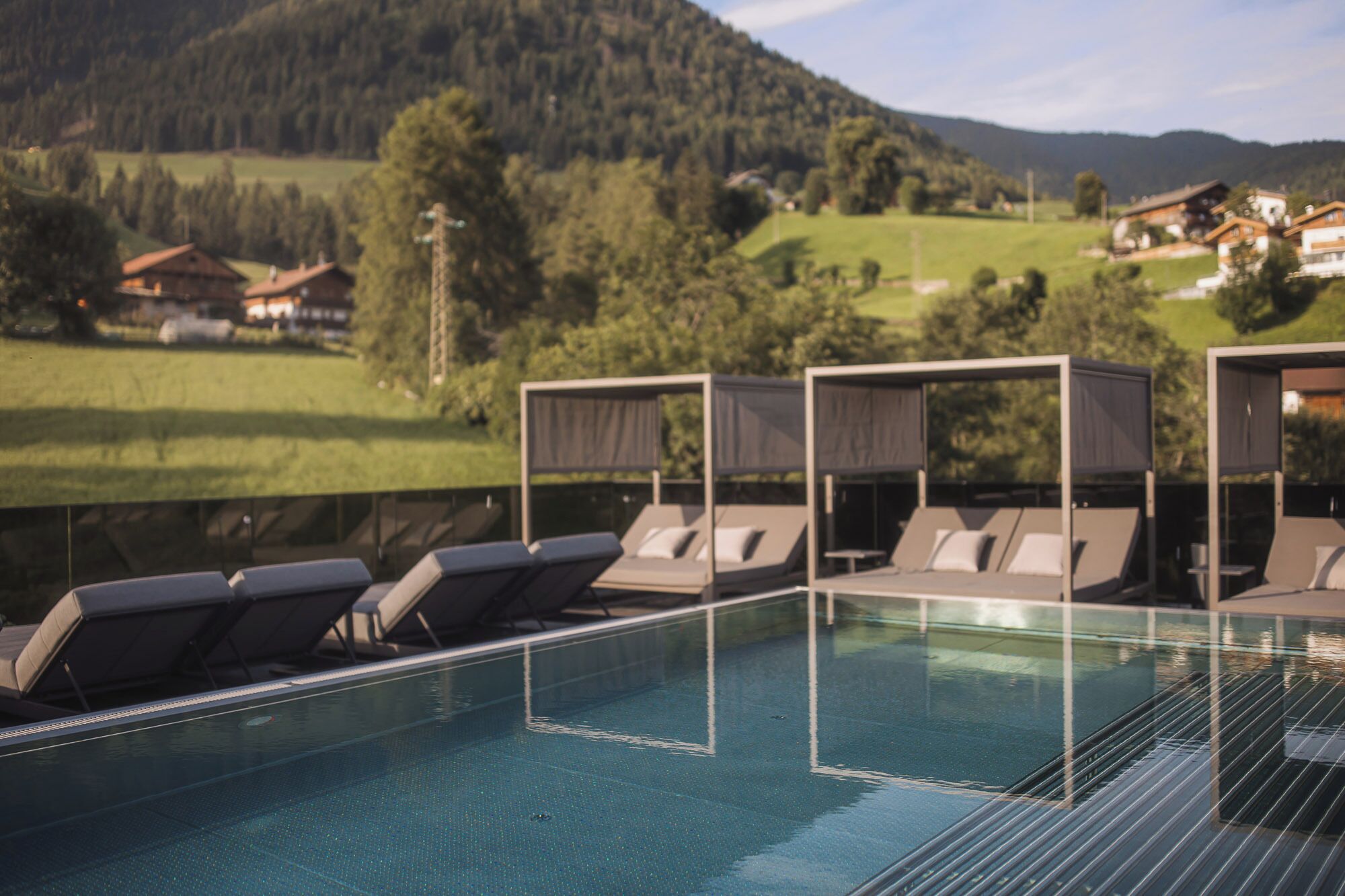 A pool area with sun loungers and a view of a mountainous landscape.