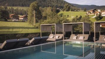 A pool area with sun loungers and a view of a mountainous landscape.
