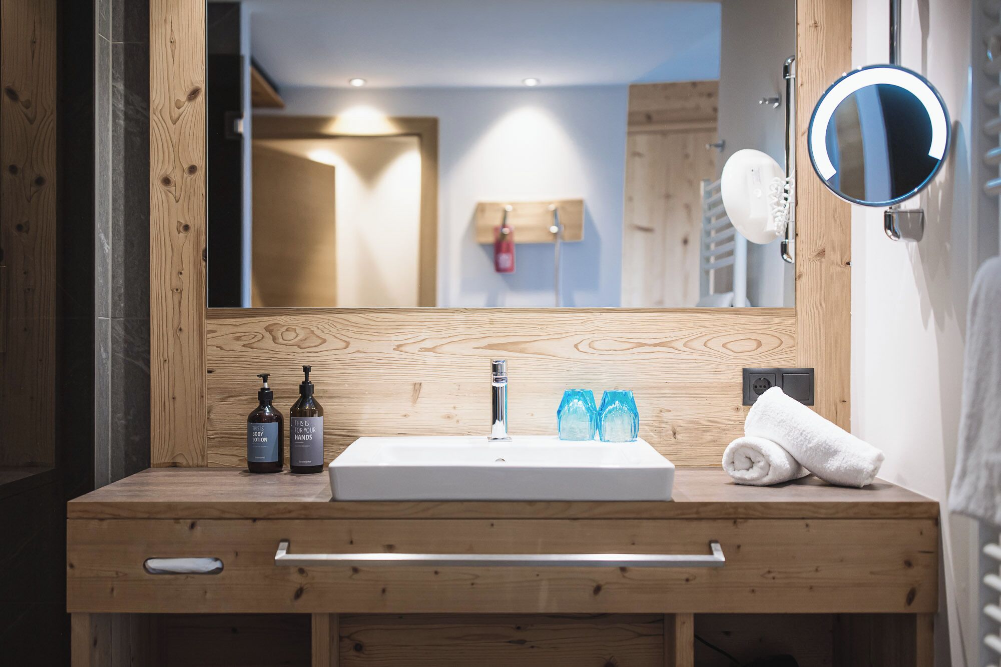 A wooden vanity with a white sink, two bottles of body lotion, and a towel.