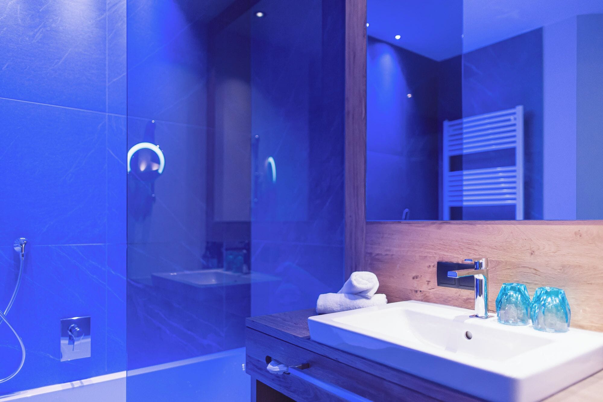 A modern bathroom with a white sink, blue glass soap bottles, and a wooden vanity.