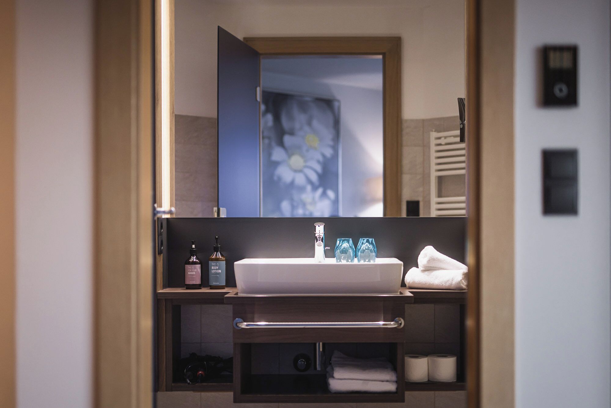 A bathroom with a white sink, a mirror, and a towel rack. There are two bottles of lotion on the shelf.