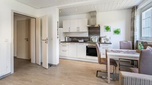 Una cocina moderna con armarios blancos, horno empotrado y comedor con mesa y sillas.