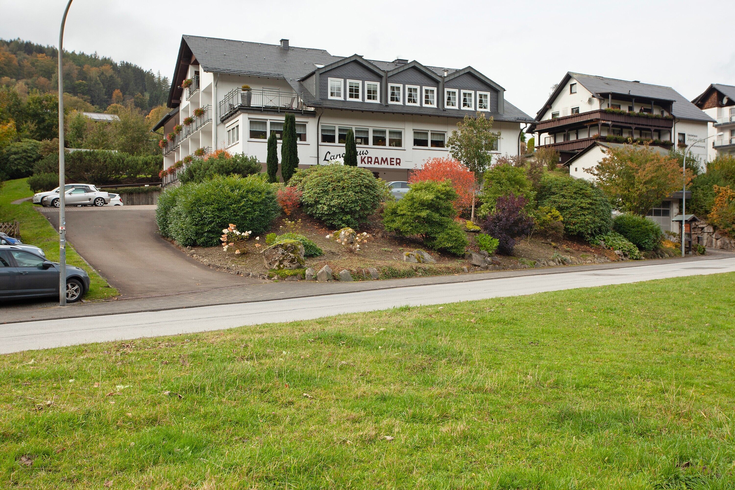 A hotel with a sign 'Langhaus KAMER' on the facade, surrounded by lush greenery and a hilly backdrop.