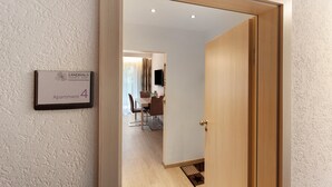 Quarto de hotel com porta de madeira, área de refeições ao fundo e uma placa indicando 'Apartamento 4'.