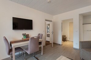 A modern living room with a flat-screen TV, a dining table with chairs, a sofa, and a hallway leading to another room.