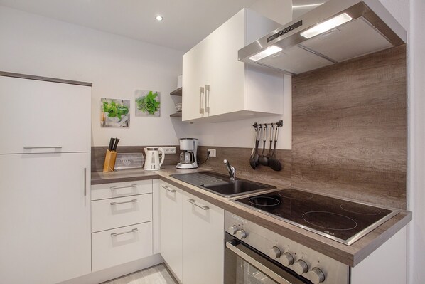 A modern kitchen with white cabinets, a built-in oven, a stovetop, and a coffee maker.