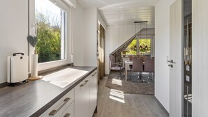 A modern kitchen with a large window, a dining area with a table and chairs, and a staircase leading to an upper level.