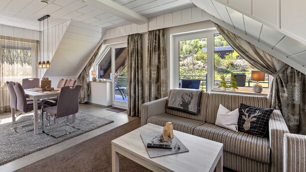 A cozy loft-style room with a dining area, a sofa, and a window with curtains.