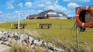 Een gebouw met een schuin dak, twee banken en een reddingsboei op een grasheuvel.