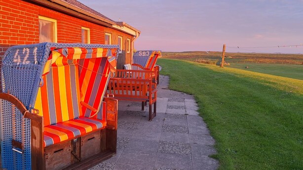 Een gebouw van rode bakstenen met een terras, waar een blauwe geweven stoel en een kleurrijke gestreepte bank staan.