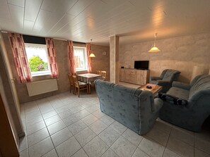 A compact living space with a sofa, a dining table, and a TV. - Apartment 'Ferienwohnung Uthlande' with Shared Terrace, Shared Garden and Wi-Fi (Langeneß)