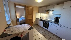 Cozinha compacta com fogão, forno e pia, porta de madeira e painel de azulejos.