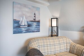 Una habitación con un sofá, un cuadro de un faro y veleros, y una lámpara de pie.