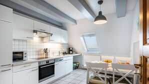 Una cocina moderna con armarios blancos, horno empotrado y comedor con mesa y sillas.