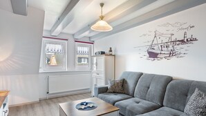 Un salón moderno con un sofá gris, una mesa de centro de madera, un radiador y un mural en la pared con la imagen de un barco.