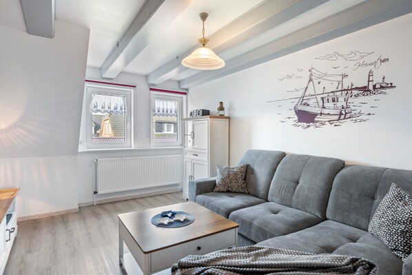 Sala de estar moderna com sofá cinzento, mesa de centro de madeira, radiador e painel na parede com ilustração de barco.