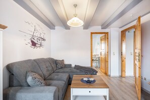 Uma sala de estar moderna com um sofá cinza, uma mesa de centro de madeira e uma ilustração de um navio na parede.