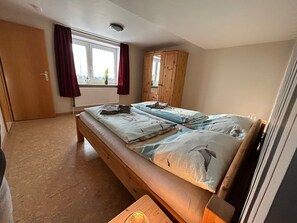 A bedroom with a bed, a wooden wardrobe, a window with curtains, and a radiator.