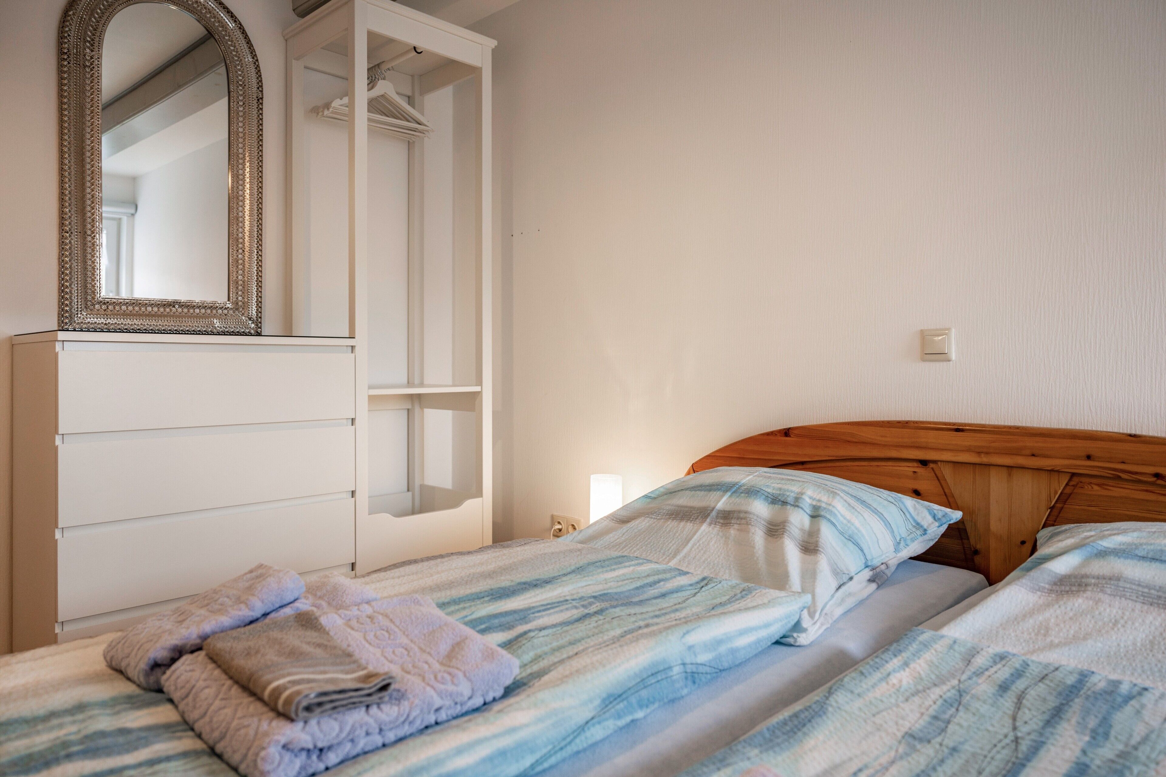 A bedroom with a bed, a wooden headboard, a white dresser, and a mirror.