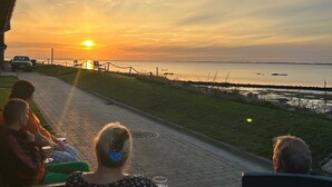 Ein Sonnenuntergangsblick von einer Terrasse mit einem gepflasterten Weg, einer Rasenfläche und einem Gewässer im Hintergrund.