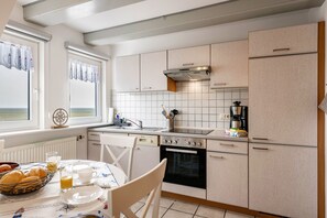 Une cuisine équipée d’une table à manger, de chaises, d’une machine à café et offrant une vue sur la mer par la fenêtre.