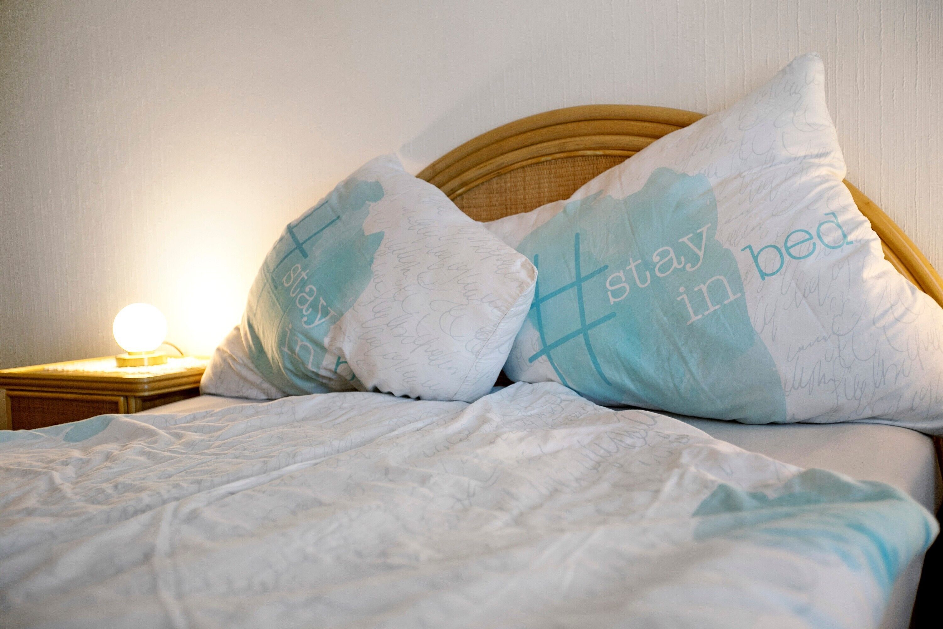 Una cama con cabecera, dos almohadas con texto y una lámpara de noche.