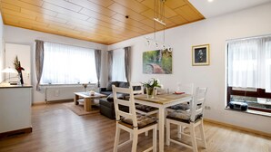 Una sala de estar moderna con techo de madera, una mesa de comedor con sillas, un sofá, una mesa de centro y una ventana con cortinas.