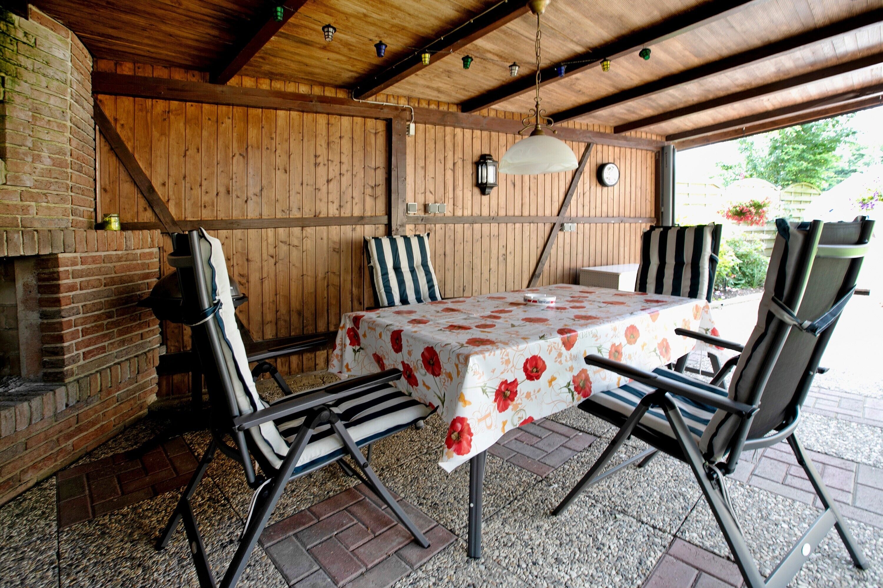 An outdoor patio with a table, chairs, a brick fireplace, and wooden walls.